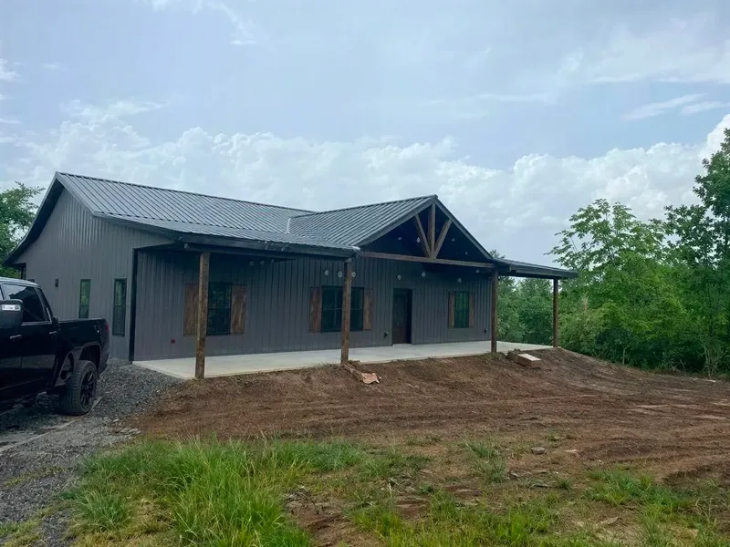 Gray barndominium with a timber-framed gabled front porch during construction