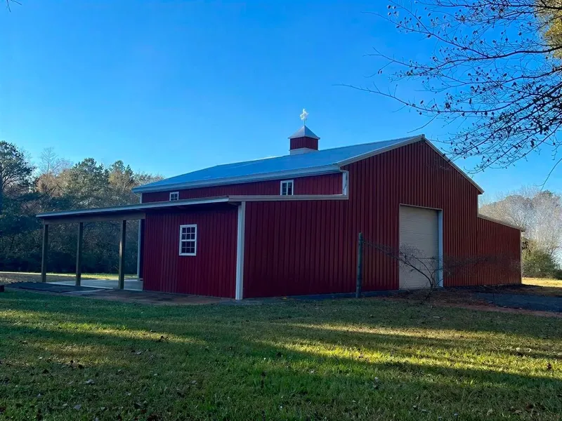 Red barndominium with white trim, a cupola, and a covered side porch