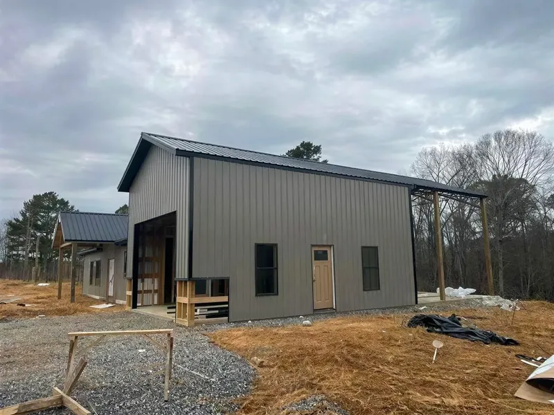 Gray metal barndominium under construction with tall windows and an open garage bay