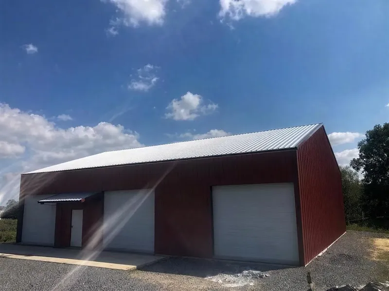 Red metal barndominium with a covered porch and two garage doors